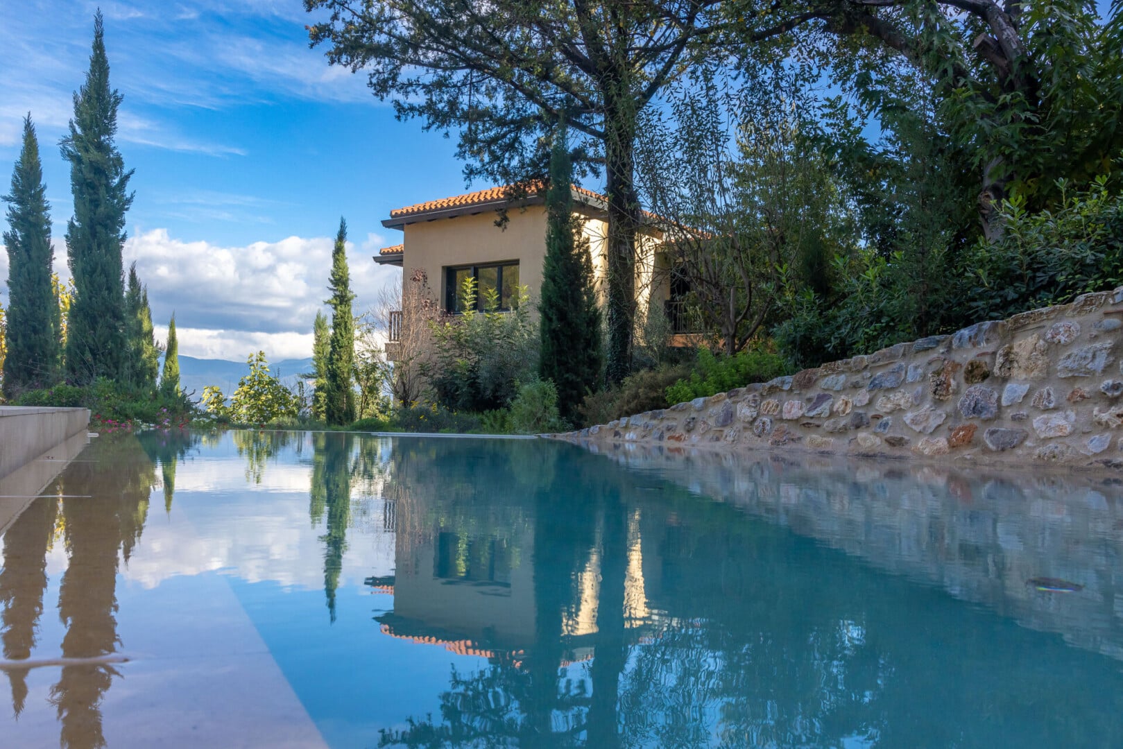 Image taken from the surface level of the rectangular pool at Euphoria Retreat showing the reflections of the sky, building and trees in the still waters.